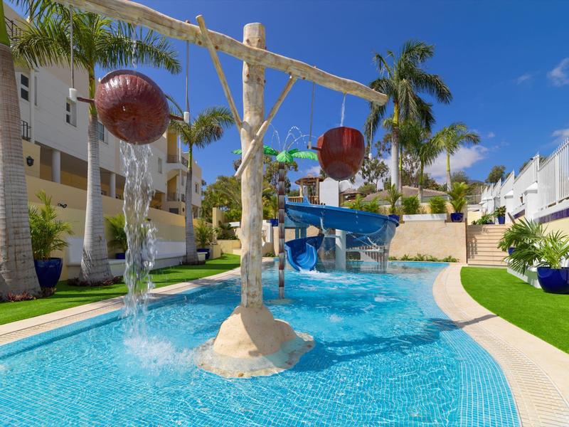 Wasserspiel mit fließendem Wasser, Rutschen und Palmen in einem blauen Poolbereich.