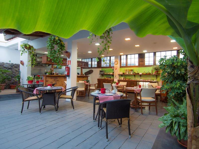 Terrasse d'hôtel accueillante avec tables, chaises et végétation luxuriante.