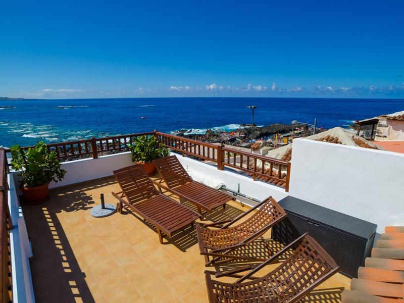 Terrasse sur le toit avec chaises longues, plantes et vue sur la mer sous un ciel dégagé.