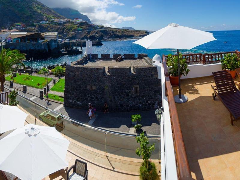 Balcon avec chaises longues, parasol et vue sur la mer et la côte sous un ciel clair.