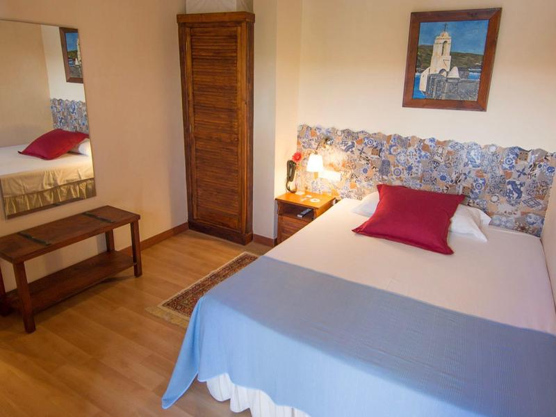 Chambre confortable avec lit double, literie bleue et rouge, coiffeuse avec miroir et porte en bois.