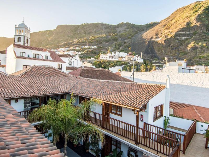 Village avec maisons blanches et clocher d'église devant un paysage montagneux ensoleillé.