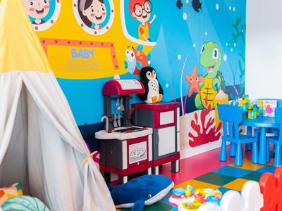 Bunter Kinderspielraum mit Tipi, Spielküche, blauem Tisch und Stühlen vor einer Wand mit Tiermotiven.