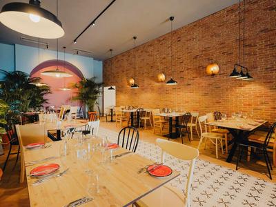 Modernes Restaurant mit Backsteinwand, Holztischen, Pflanzen und warmem Licht für gemütliche Atmosphäre.
