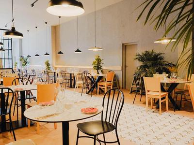 Helles Café mit Tischen, Stühlen und Pflanzen an den Wänden