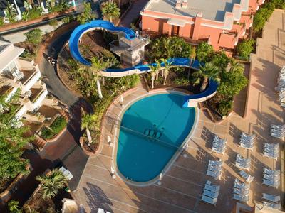 Blick von oben auf einen Pool mit Wasserrutsche und Liegestühlen auf einer Hotelterrasse.
