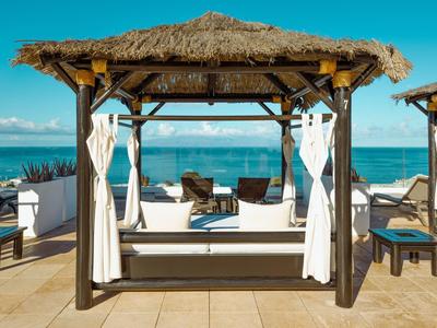 Ruhige Terrasse mit Loungesesseln und Meerblick unter Strohdach-Pavillon