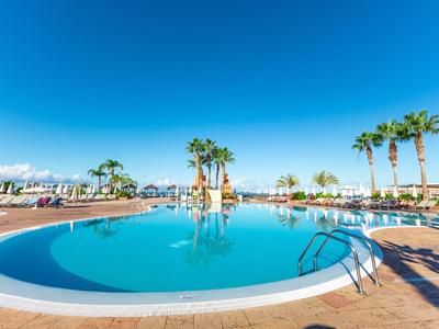 Rond buitenzwembad met ligstoelen en palmbomen onder een heldere blauwe lucht.