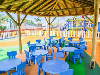 Kleurrijke kinderspeelplaats met blauwe tafels en stoelen onder een rieten dak