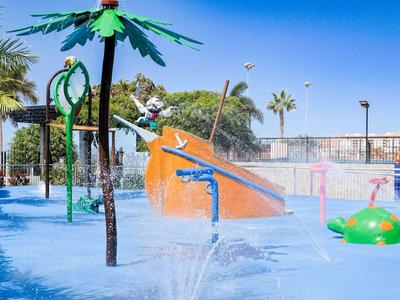 Kleurrijk waterpark met glijbaan en speelse watersproeiers onder een blauwe lucht.