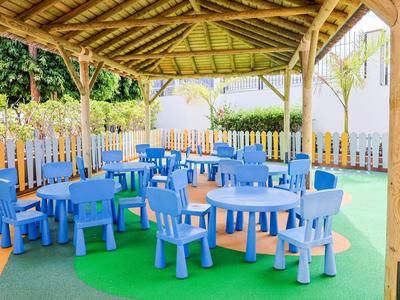 Kleurrijke speelruimte voor kinderen met blauwe tafels en stoelen onder een houten dak buiten.