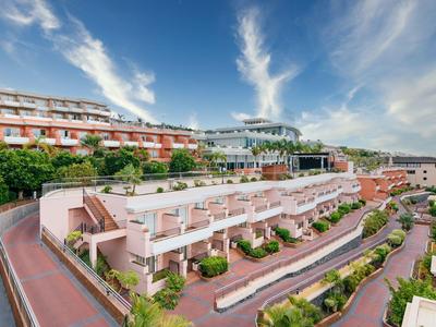 Meerdelig hotel met terrassen omgeven door groen onder een heldere hemel.