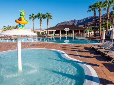Kinderzwembad met waterspeelgoed, parasols en ligstoelen bij een hotelzwembad omgeven door palmen