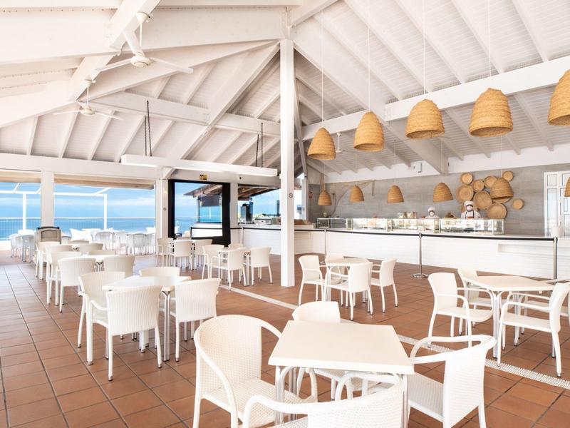 Offenes Restaurant mit weißen Möbeln und Meerblick unter einem weißen Dach.