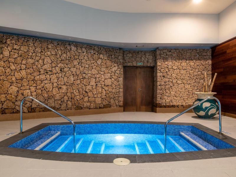 Innenbereich mit beleuchtetem Whirlpool vor Wand aus Naturstein mit Holztür