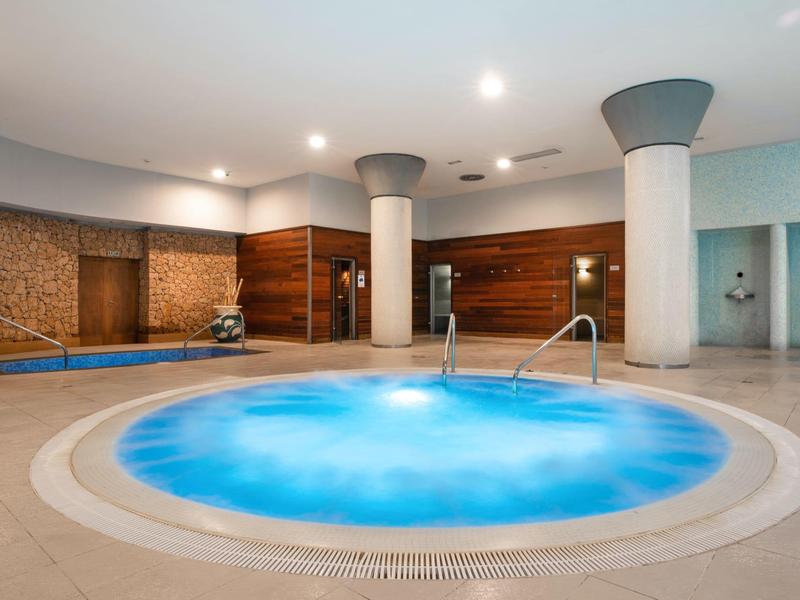 Moderner Indoor-Whirlpool in einem Wellnessbereich mit weißen Säulen und Holzwänden.