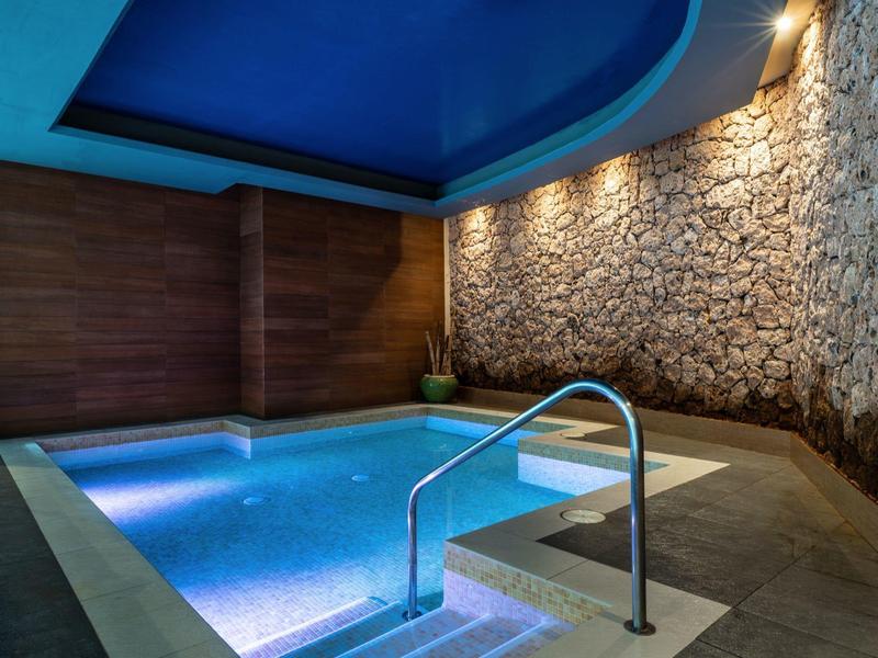 Innenpool mit Beleuchtung in einem modernen Wellnessbereich mit Steinwand und Holzdecke