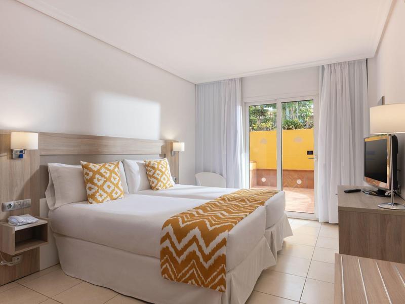 Modernes Hotelzimmer mit Doppelbett, gelben Akzenten und Zugang zu einer Terrasse.