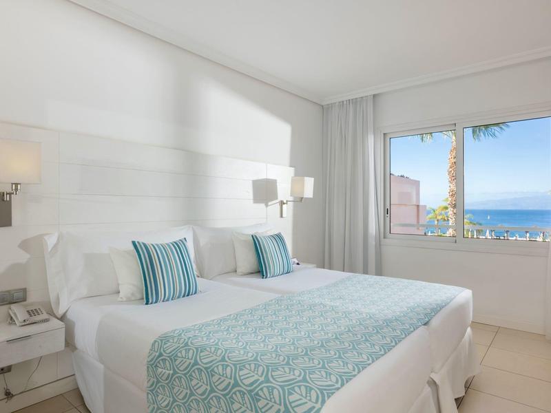 Helles Hotelzimmer mit Doppelbett, weißen Wänden und Meerblick durch das Fenster.