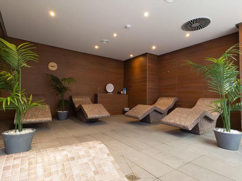 Ruheraum mit Holzverkleidung, gepolsterten Liegen und großen Pflanzen in Töpfen.