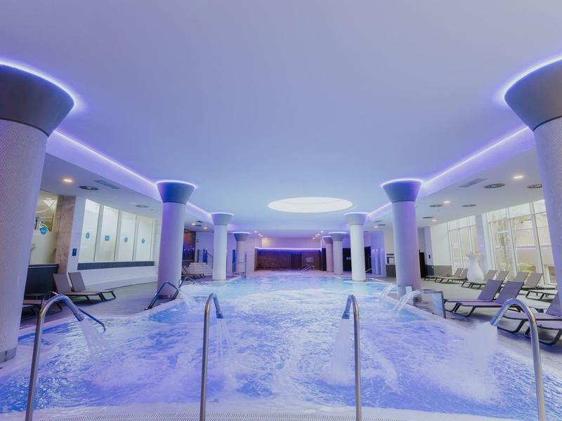 Moderner Spa-Bereich mit beheiztem Indoor-Pool, beleuchtetem Wasser und entspannenden Liegen.