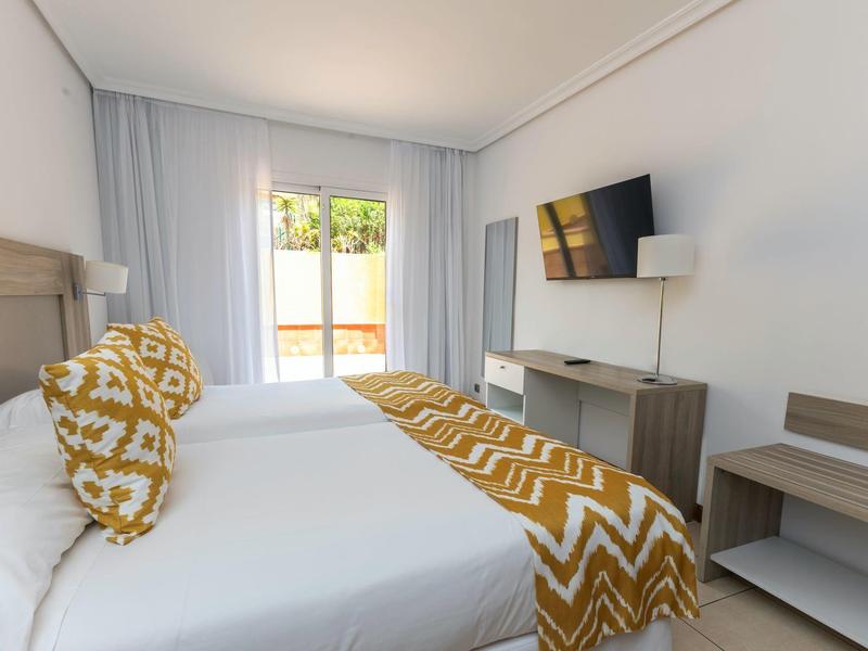 Modernes Hotelzimmer mit zwei Einzelbetten, Gelb-weißen Kissen und Decken, TV und Balkon.