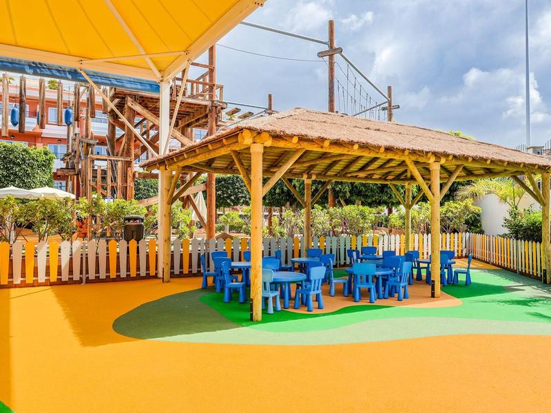 Outdoor-Sitzbereich mit blauen Stühlen und Tischen unter einem Holzpergola bei einem Hotel