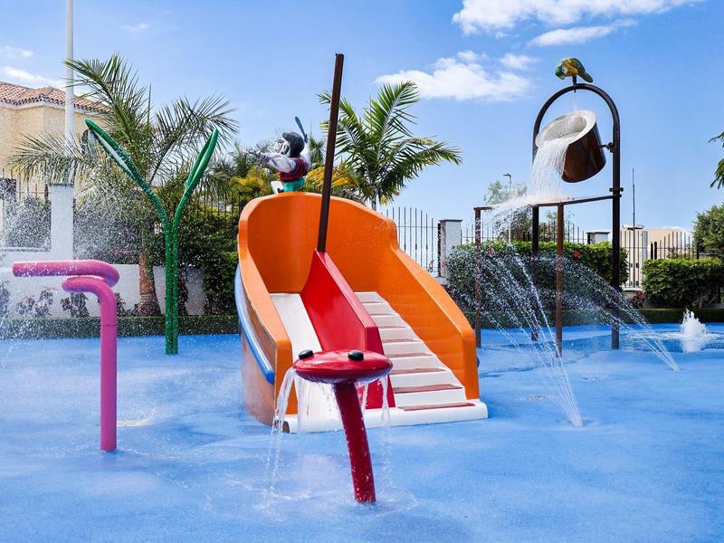 Wasserpark mit Wasserrutsche, Fontänen und Palmen unter blauem Himmel