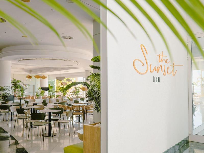 Moderner, heller Hotel-Loungebereich mit Pflanzen und vielen Stühlen und Tischen.