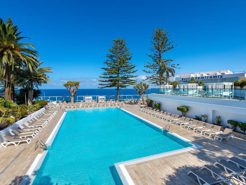Piscina clara en un día soleado con palmeras y vista al mar en el fondo.