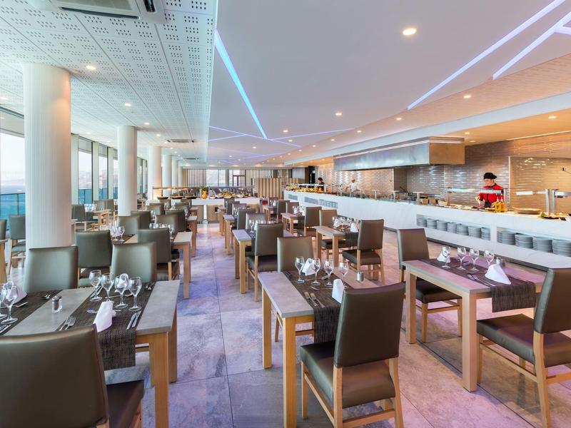 Restaurante moderno de hotel con mesas elegantemente preparadas y grandes ventanales con vista al mar.