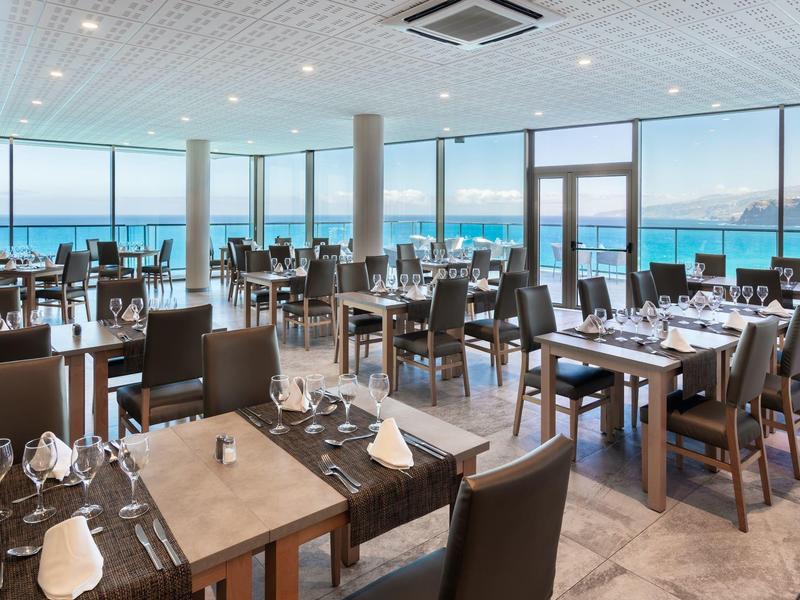 Restaurante moderno de hotel con sillas y mesas de madera, gran ventanal con vista al mar.