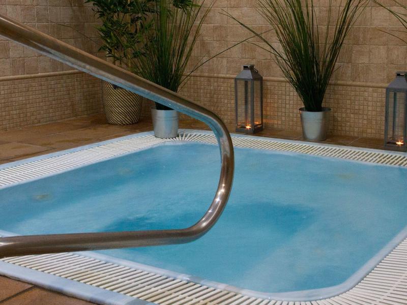 Pequeña piscina con barandilla de acero inoxidable y plantas en macetas en un rincón tranquilo.