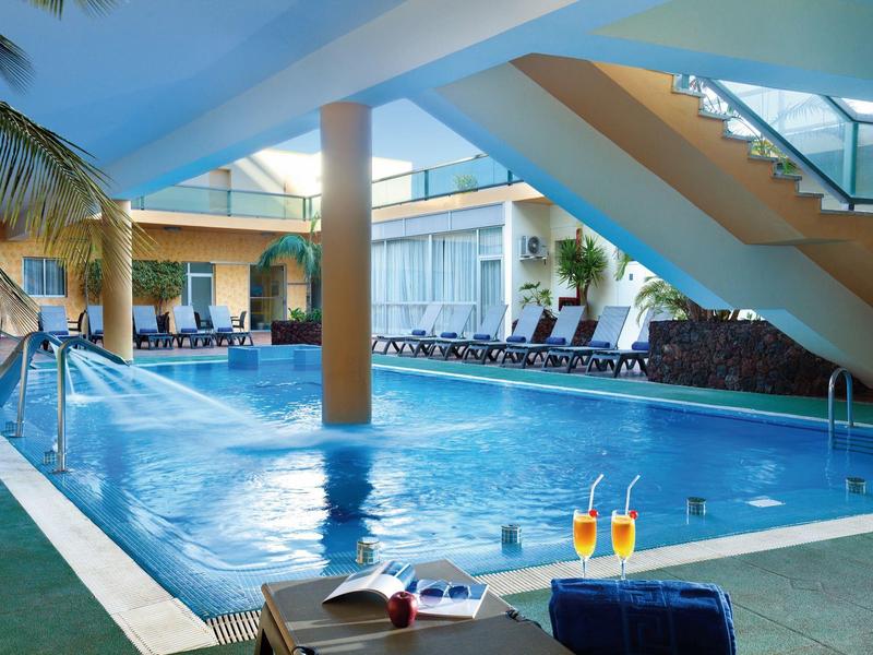 Piscina cubierta con hamacas y bebidas, ambiente relajante en un hotel moderno.
