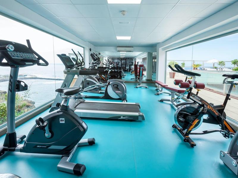 Gimnasio luminoso con equipo moderno y grandes ventanas con vista al mar.