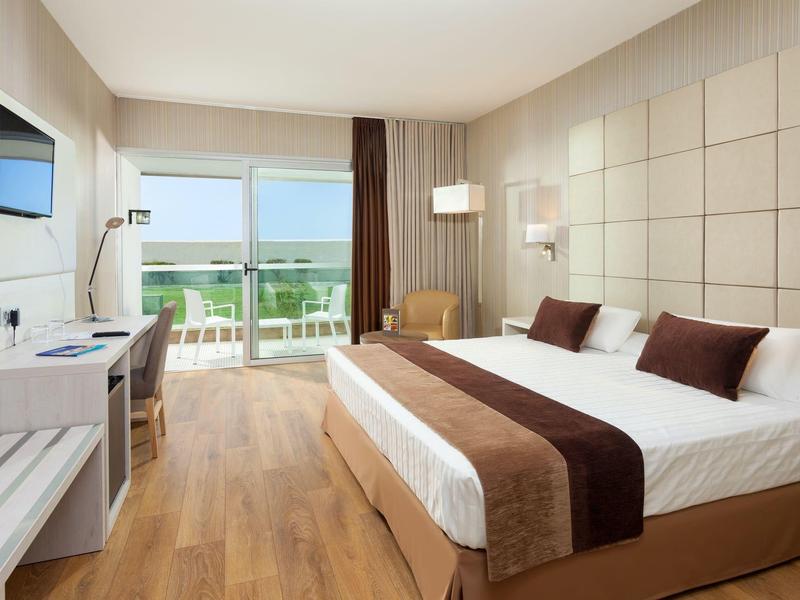 Habitación de hotel moderna con cama doble, escritorio, televisor y balcón con vista al mar.