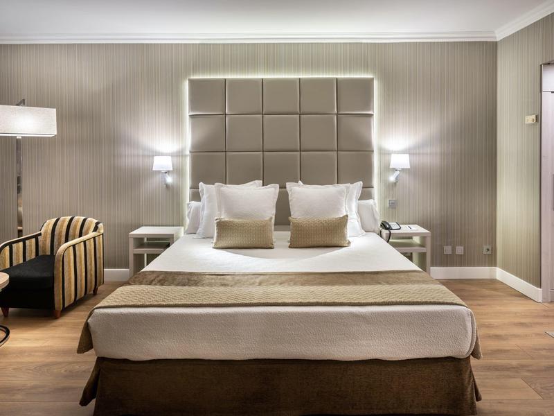 Habitación de hotel elegante con cama grande, sillones cómodos y luz cálida.