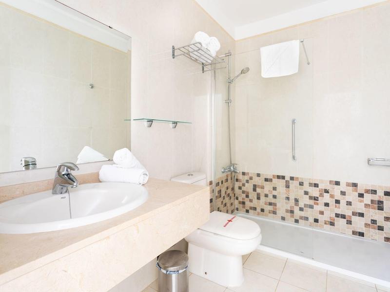 Salle de bain lumineuse avec lavabo blanc, toilettes, baignoire et zone carrelée.