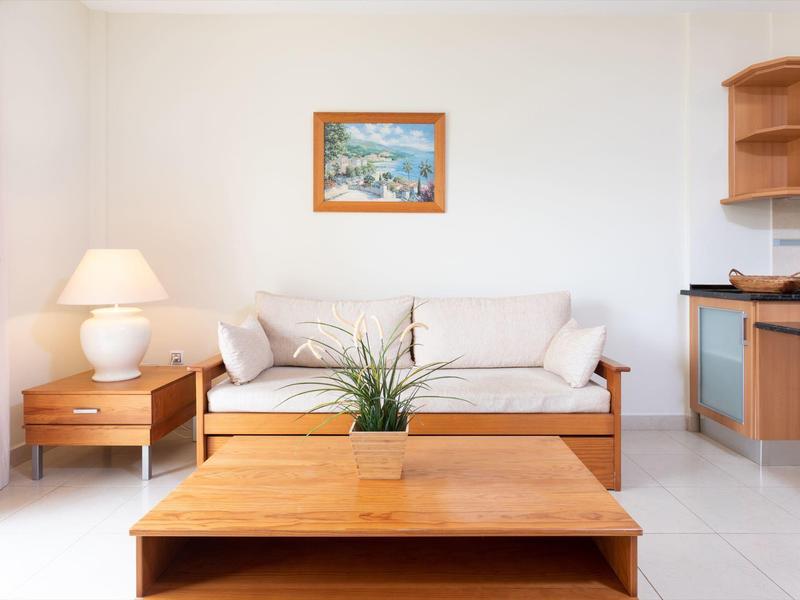 Salon lumineux avec canapé blanc, tables en bois et tableau décoratif au mur.