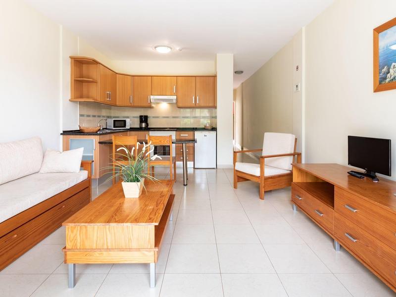 Salon lumineux avec mobilier en bois, canapé blanc et cuisine ouverte en arrière-plan.