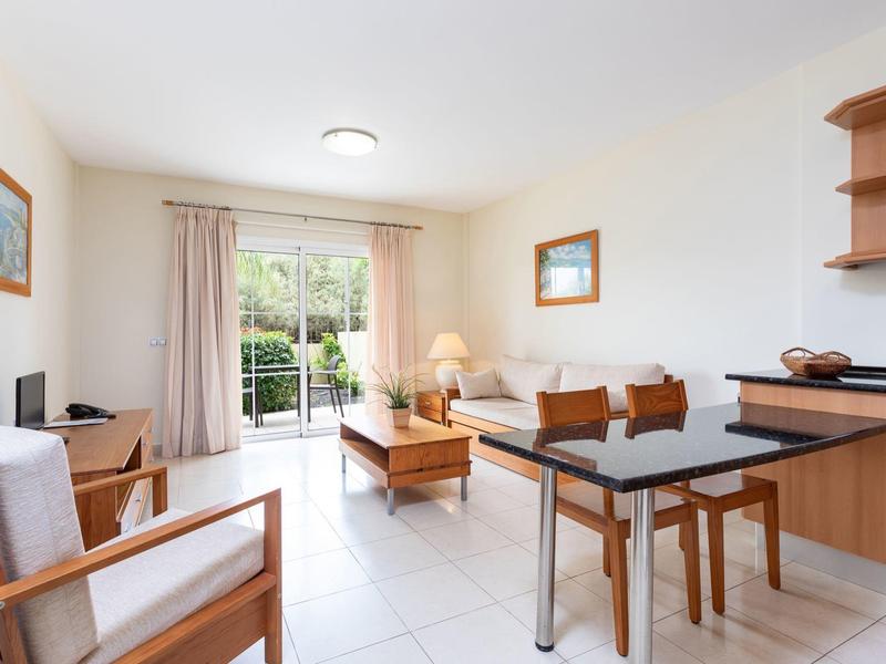 Salon lumineux avec fauteuils, table, canapé et vue sur jardin par grande porte vitrée.