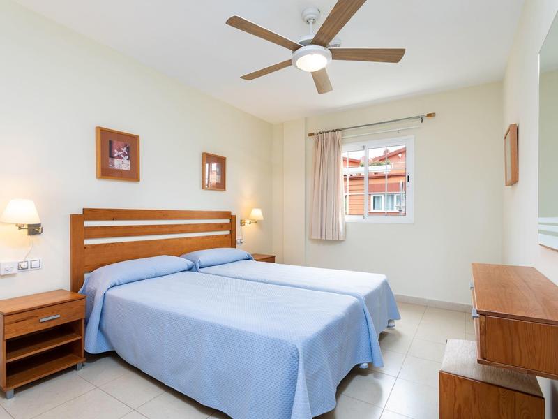 Chambre d'hôtel lumineuse avec deux lits simples, ventilateur au plafond et meubles en bois.