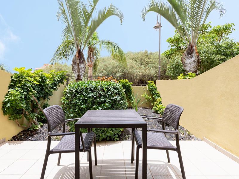 Petite terrasse avec table, quatre chaises et palmiers en arrière-plan.