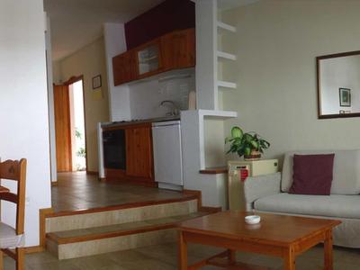 Bright living room with white sofa, wooden tables, and adjacent dining area with wooden furniture.