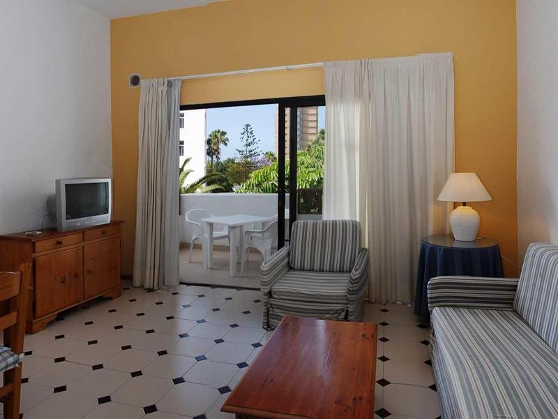 Living room with sofa, armchairs, TV, and balcony access overlooking the sea.
