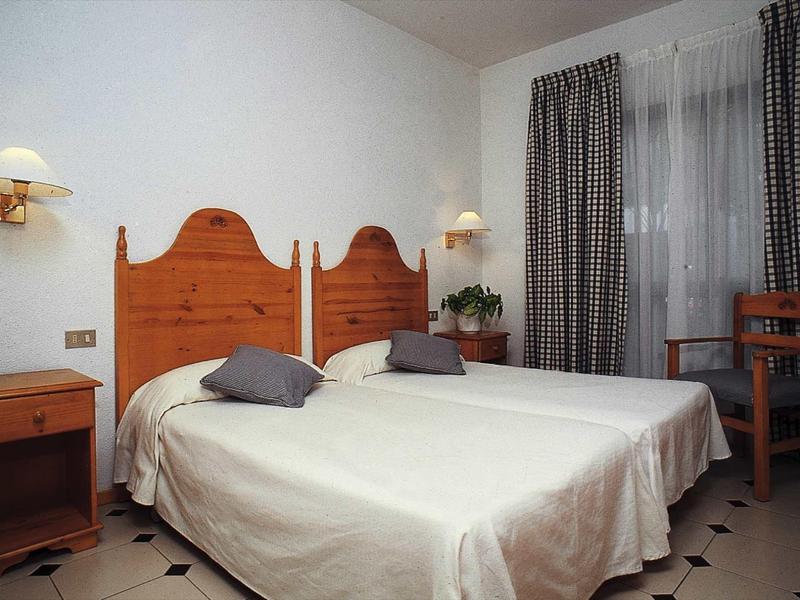 A simply furnished hotel room with two single beds, nightstand, and window with curtains.