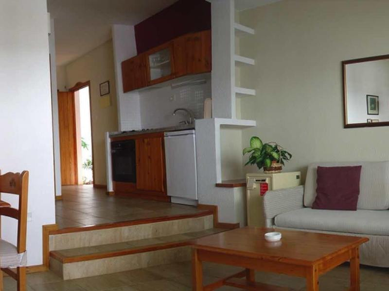 Bright living room with white sofa, wooden tables, and adjacent dining area with wooden furniture.