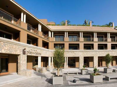 Hôtel moderne avec façade en pierre et cour sous un ciel clair.