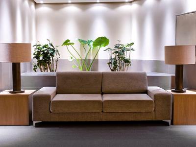 Coin salon confortable avec canapé marron, deux lampes et plantes vertes devant un mur blanc.