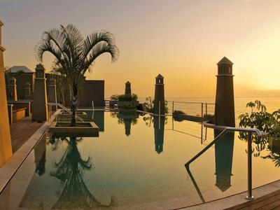 Piscine luxueuse avec vue sur la mer au coucher du soleil dans un complexe hôtelier.